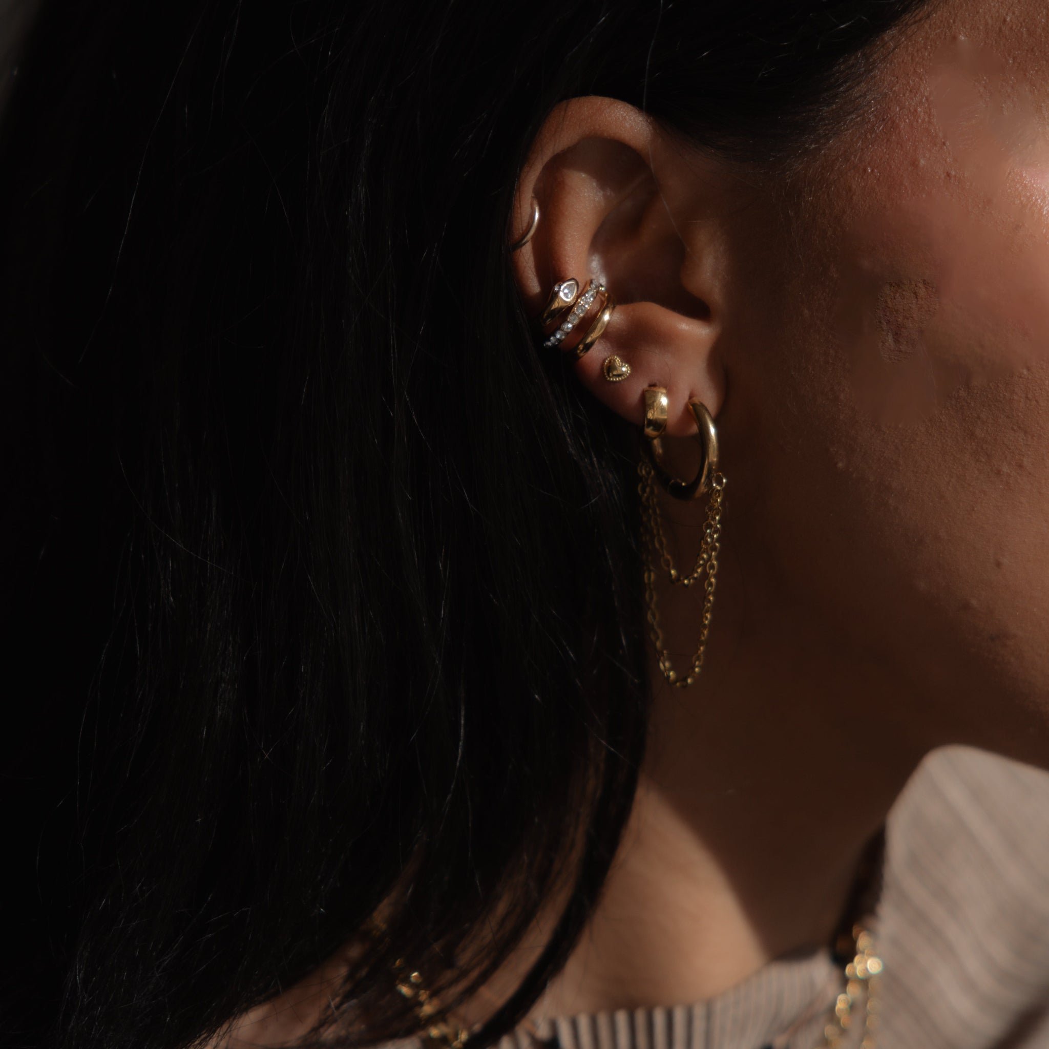 Close-up of an ear with gold hoop earrings and necklaces, blurred background