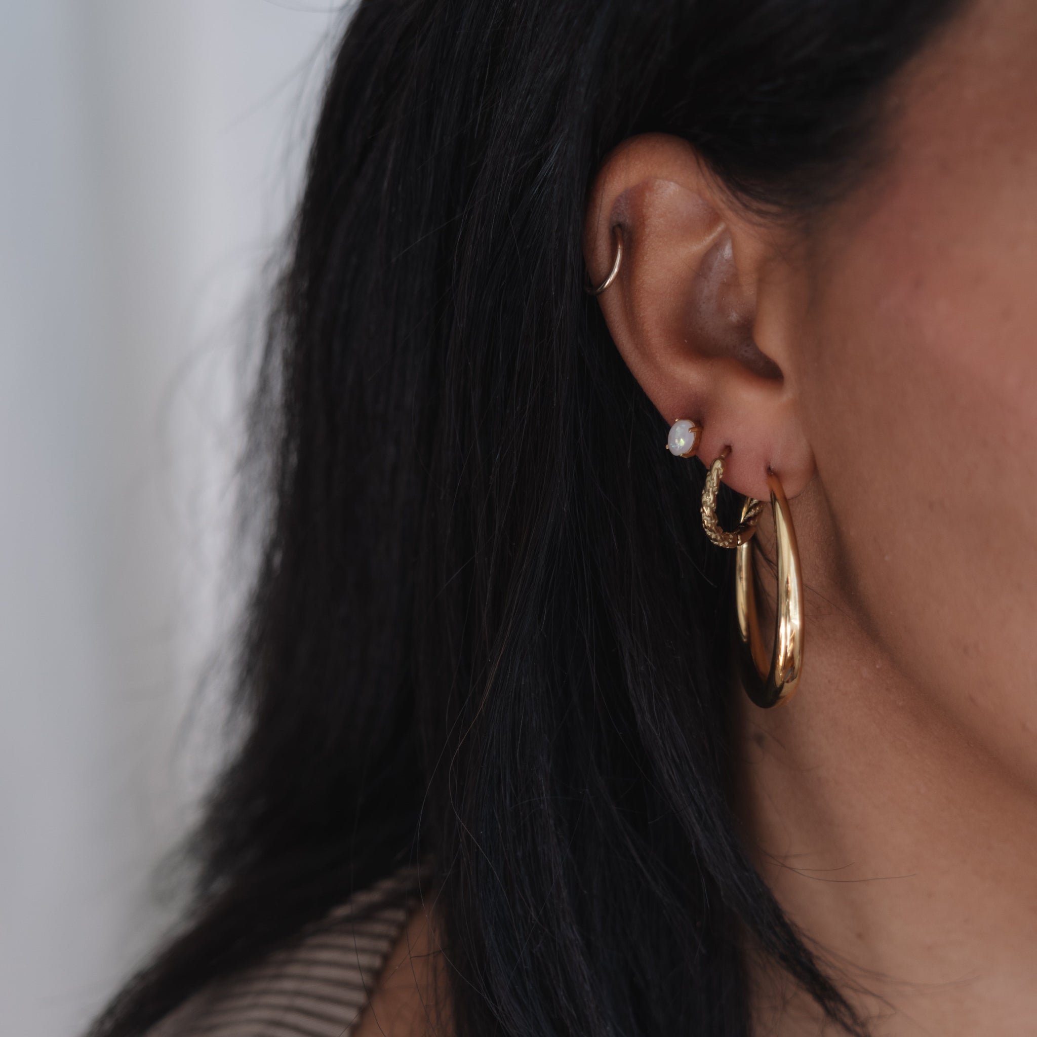 Close-up of an ear wearing gold hoop earrings with a neutral background