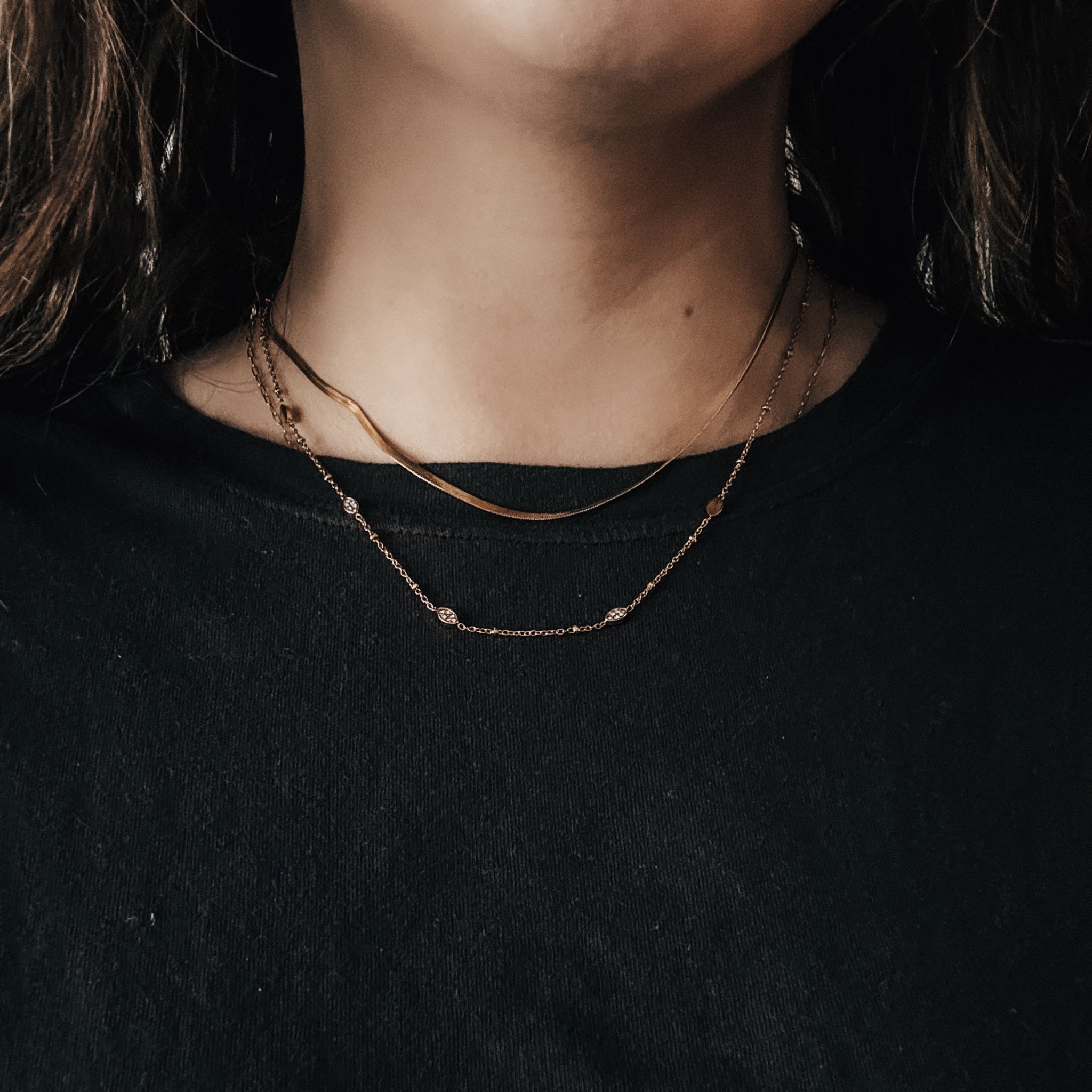 Close-up of a person wearing a delicate necklace against a dark background