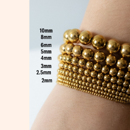 Gold beaded bracelet on a wrist with size measurement chart on a light blue background