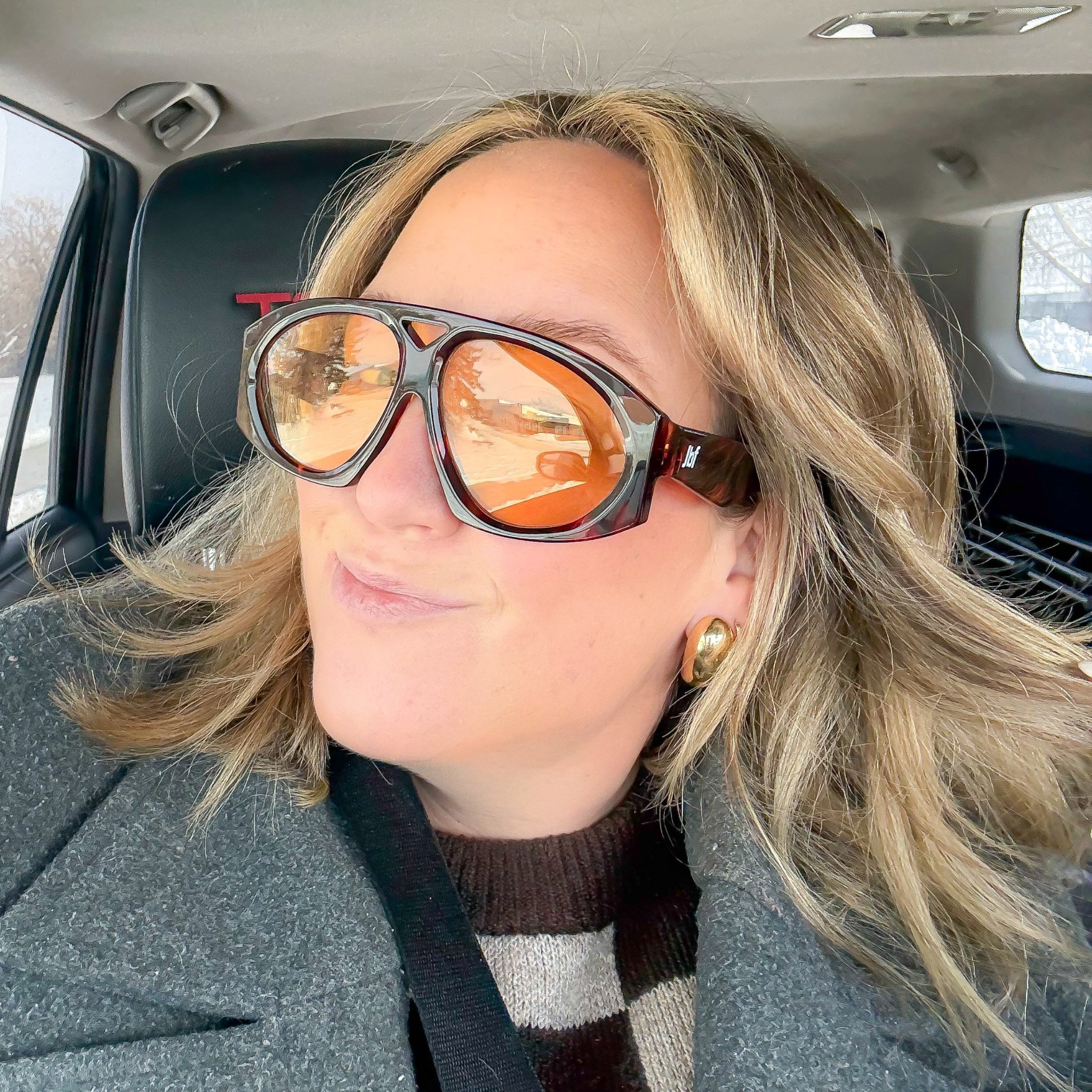 Person wearing sunglasses and a coat inside a car