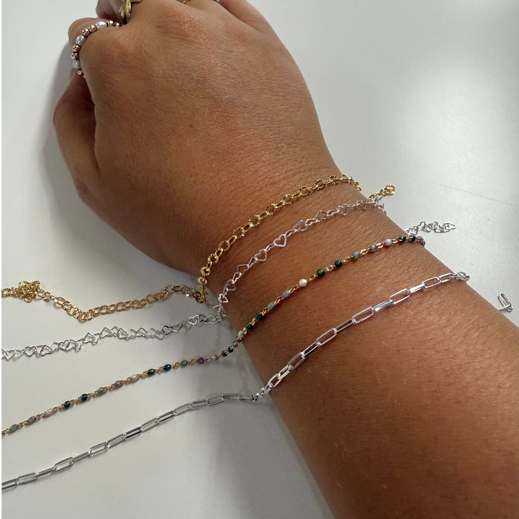 Hand wearing multiple gold and silver bracelets on a white background