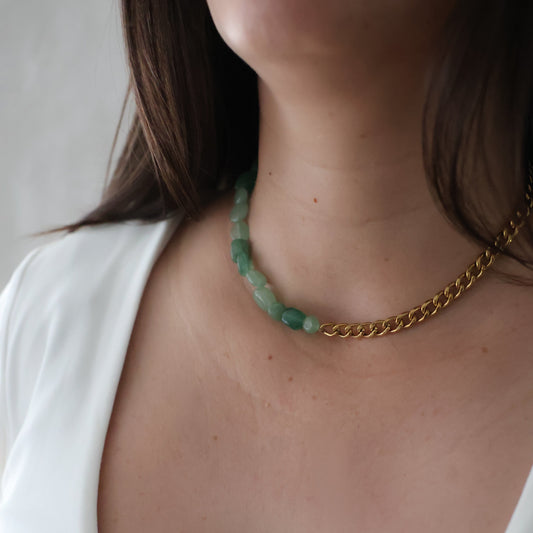 A close-up of a person wearing a necklace with green translucent beads and a gold chain, paired with a white scoop-neck top.