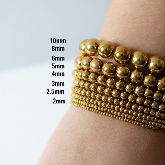 Gold beaded bracelets on a wrist with size measurements displayed.