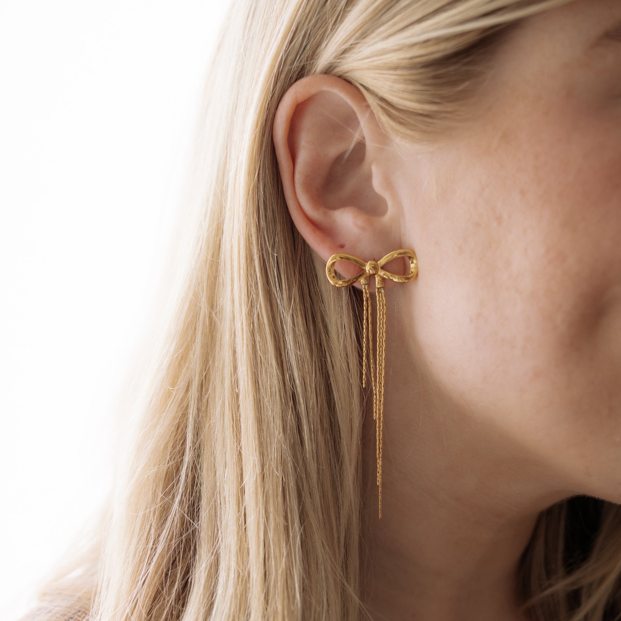 Gold bow-shaped earring worn by a person with blonde hair.
