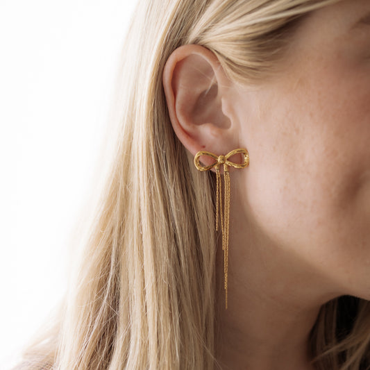 Gold bow-shaped earring worn by a person with blonde hair.