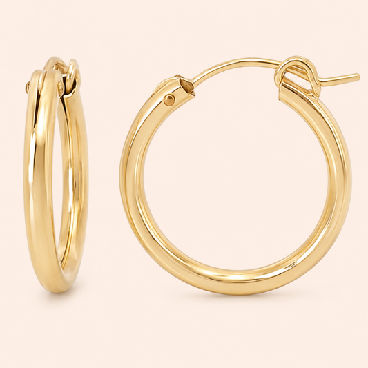 A pair of polished gold hoop earrings shown on a clean, solid pale pink background. One earring is displayed from a side profile view, and the other is shown from a front-facing angle highlighting its post and back clasp.