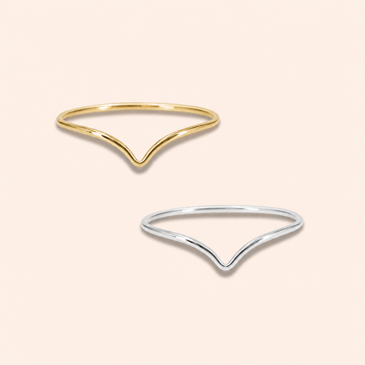 Two minimalist V-shaped open ring bangles, one in polished yellow gold and the other in polished silver, displayed on a solid pale pink background.