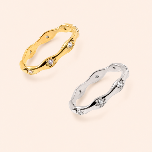 Two wavy band rings with small star-shaped diamond accents, shown on a light beige background. One ring is yellow gold and the other is silver.