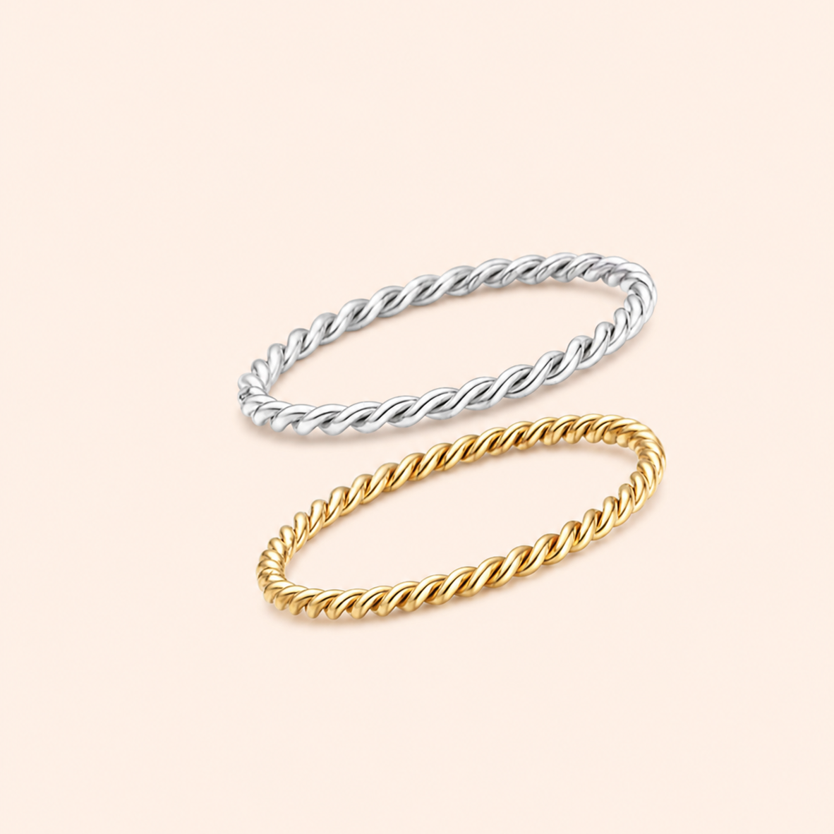 Two twisted rope-style bangles, one silver-toned and one gold-toned, arranged diagonally on a solid pale peach background.