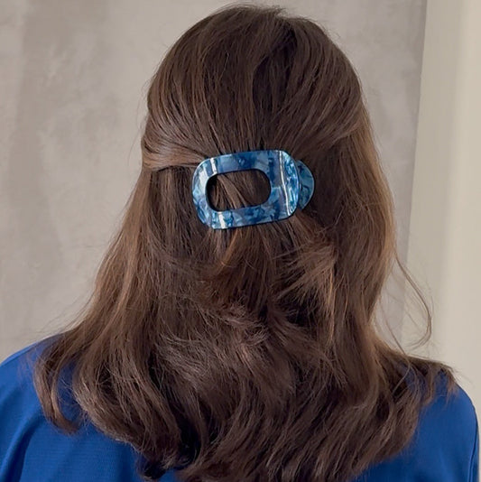 Person wearing a blue shirt with a blue hair clip in their hair against a neutral background