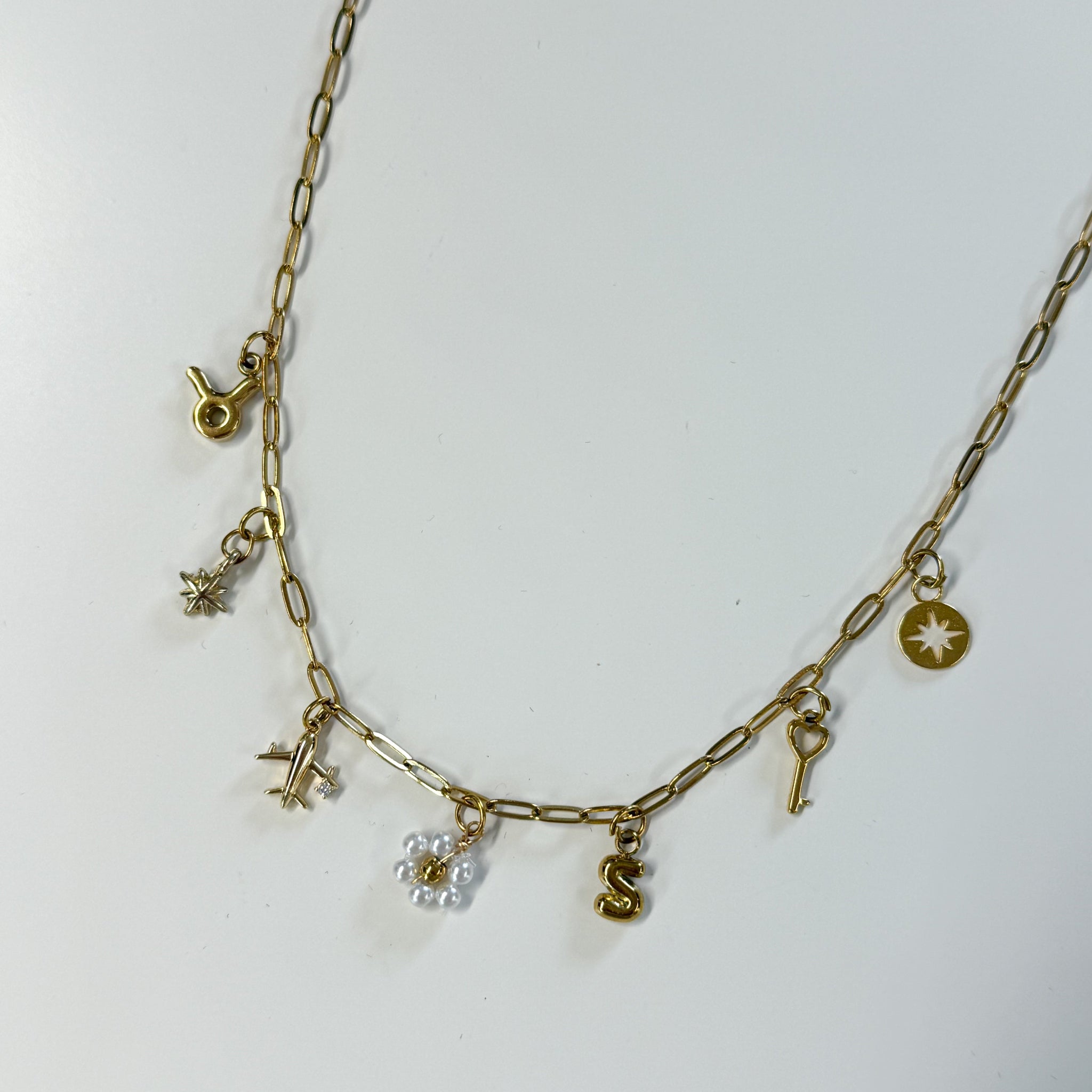 Gold necklace with various charms on a white background