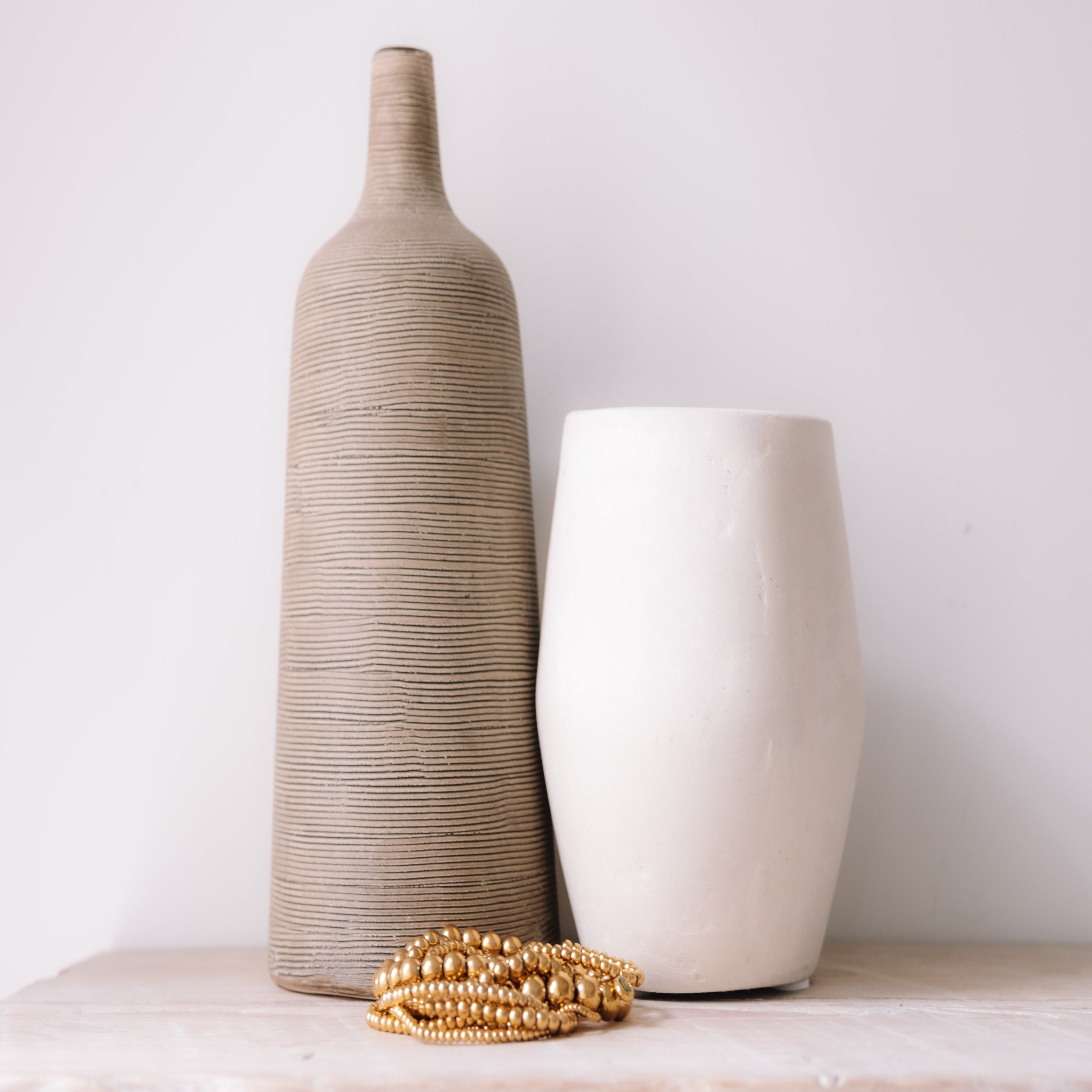 Two ceramic vases and a gold bracelet on a light surface with a white background