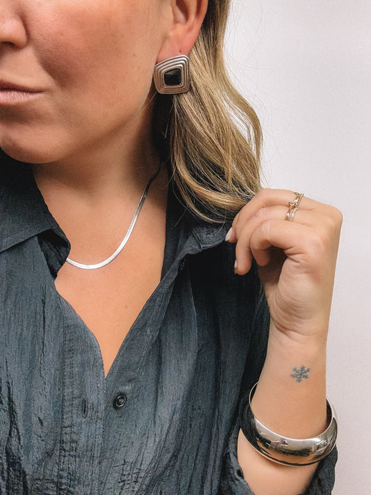 Person wearing earrings, a necklace, and bracelets on a plain background