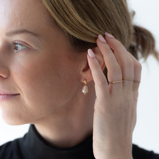 Woman wearing pearl earrings and a ring, with a blurred background