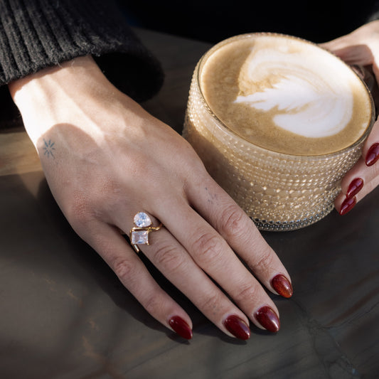 Hand with a ring holding a cappuccino cup on a wooden surface