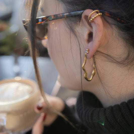 Close-up of a person wearing gold hoop earrings with a blurred background