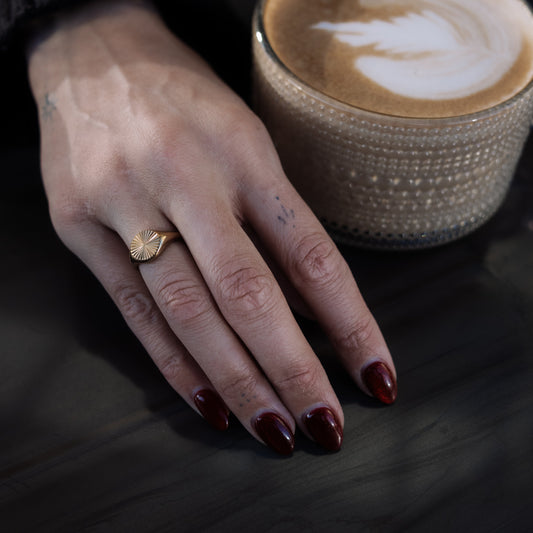 Hand with a ring holding a cup of coffee with latte art on a dark surface