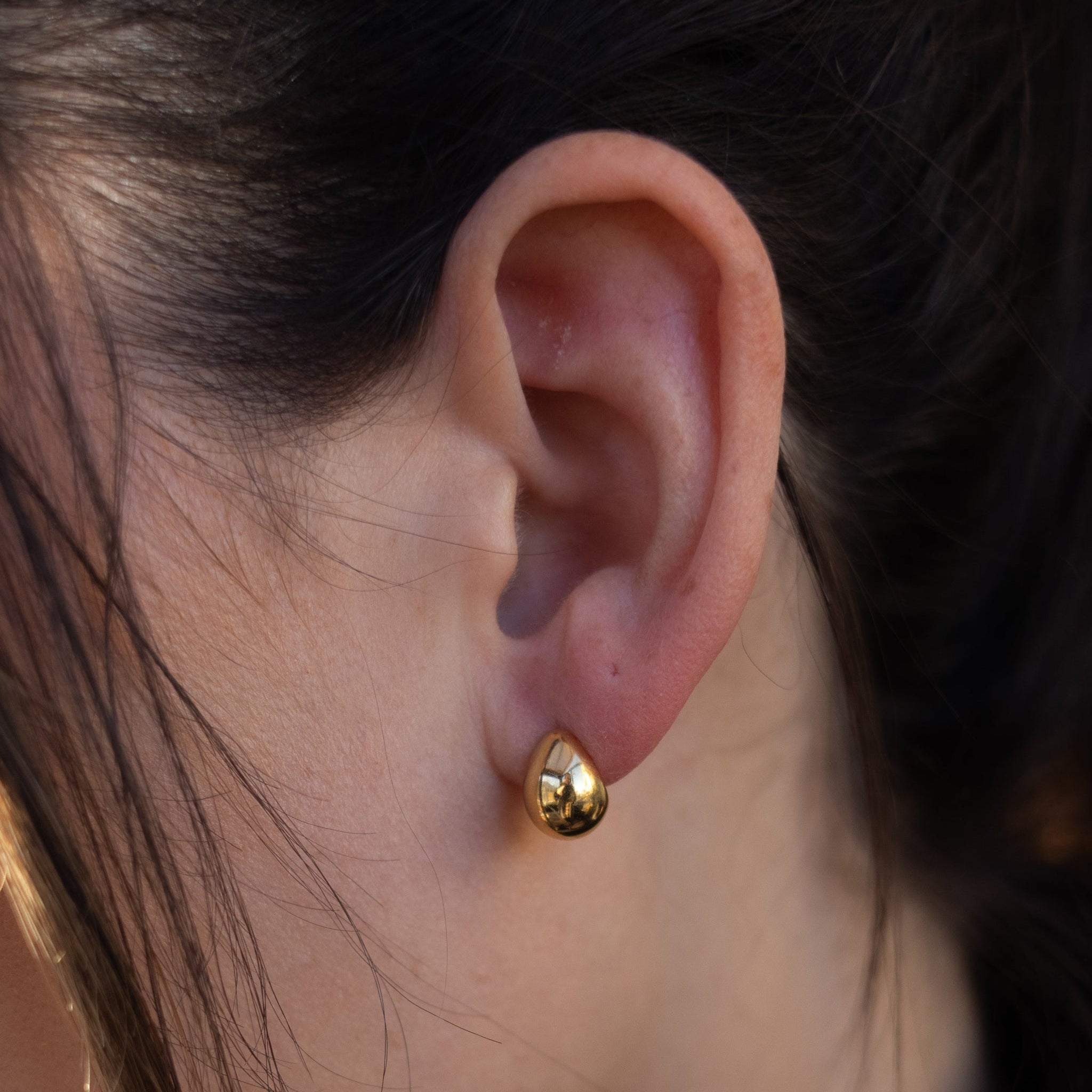 Close-up of a person wearing a gold earring with a blurred background
