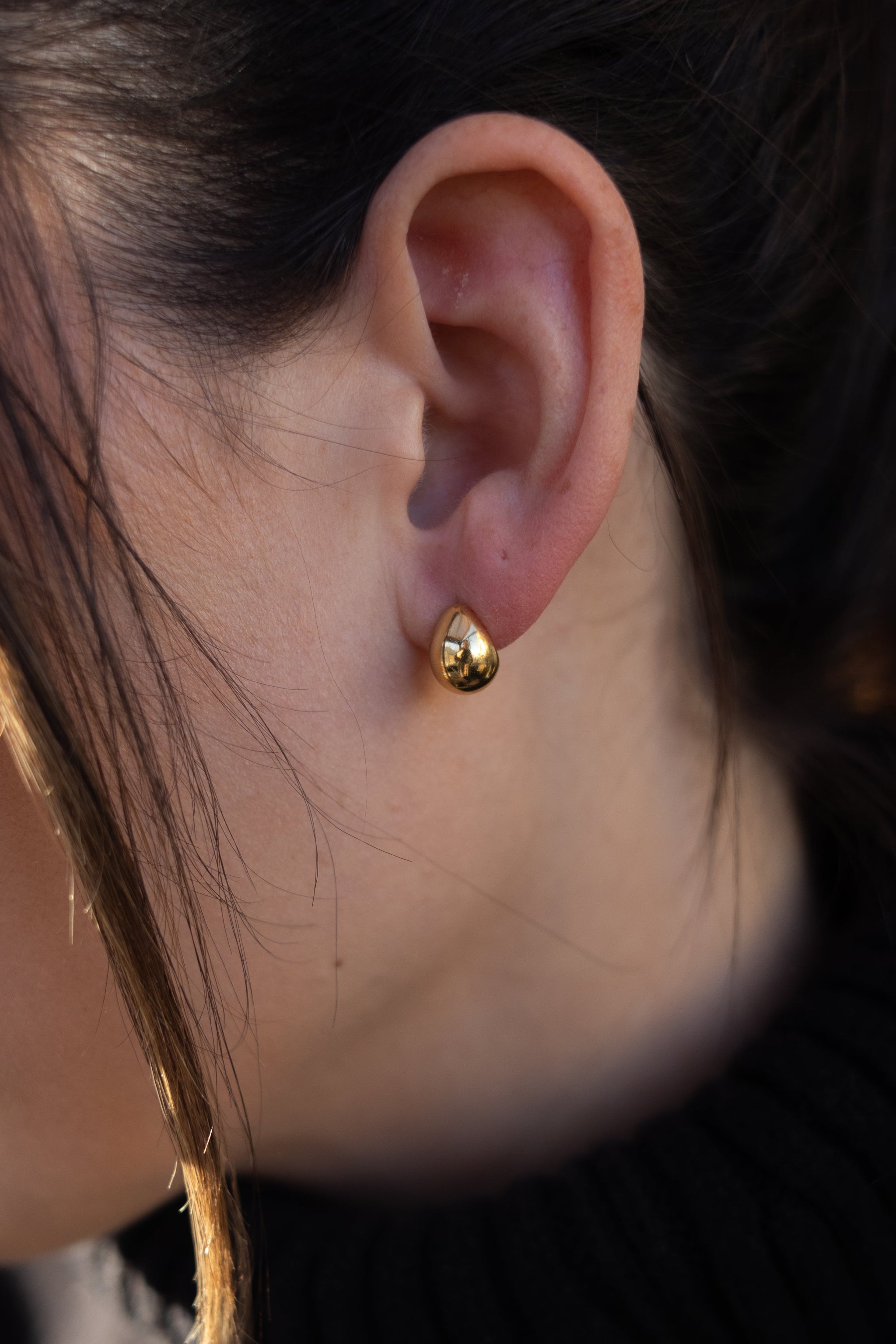 Close-up of a person wearing a gold earring with a blurred background