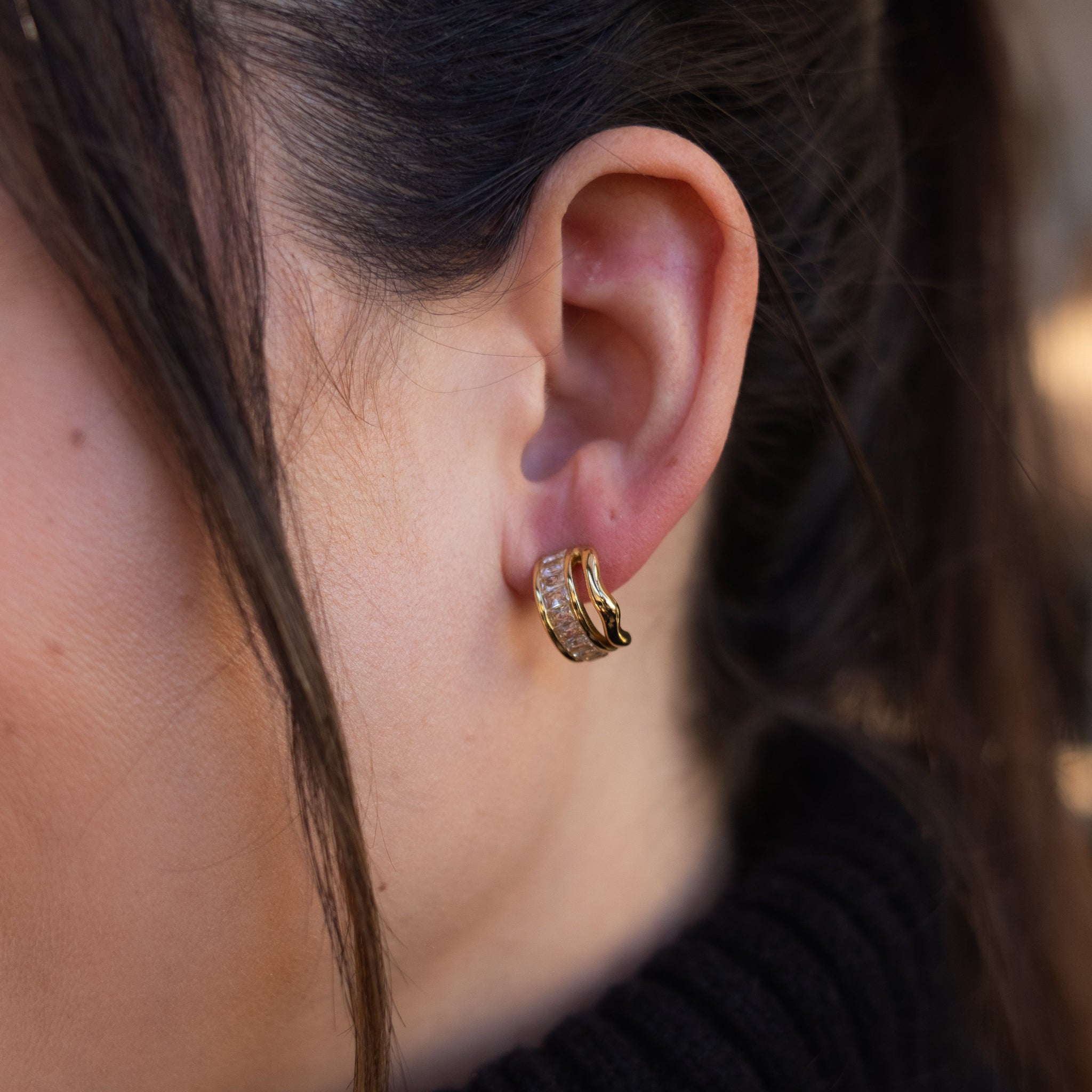 Close-up of an ear wearing a gold hoop earring with a blurred background