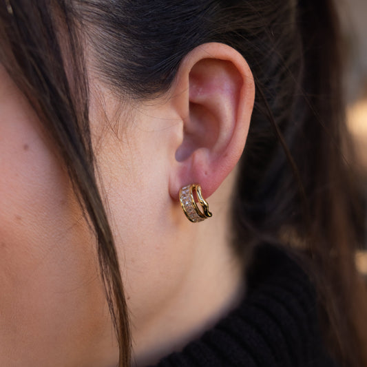 Close-up of an ear wearing a gold hoop earring with a blurred background