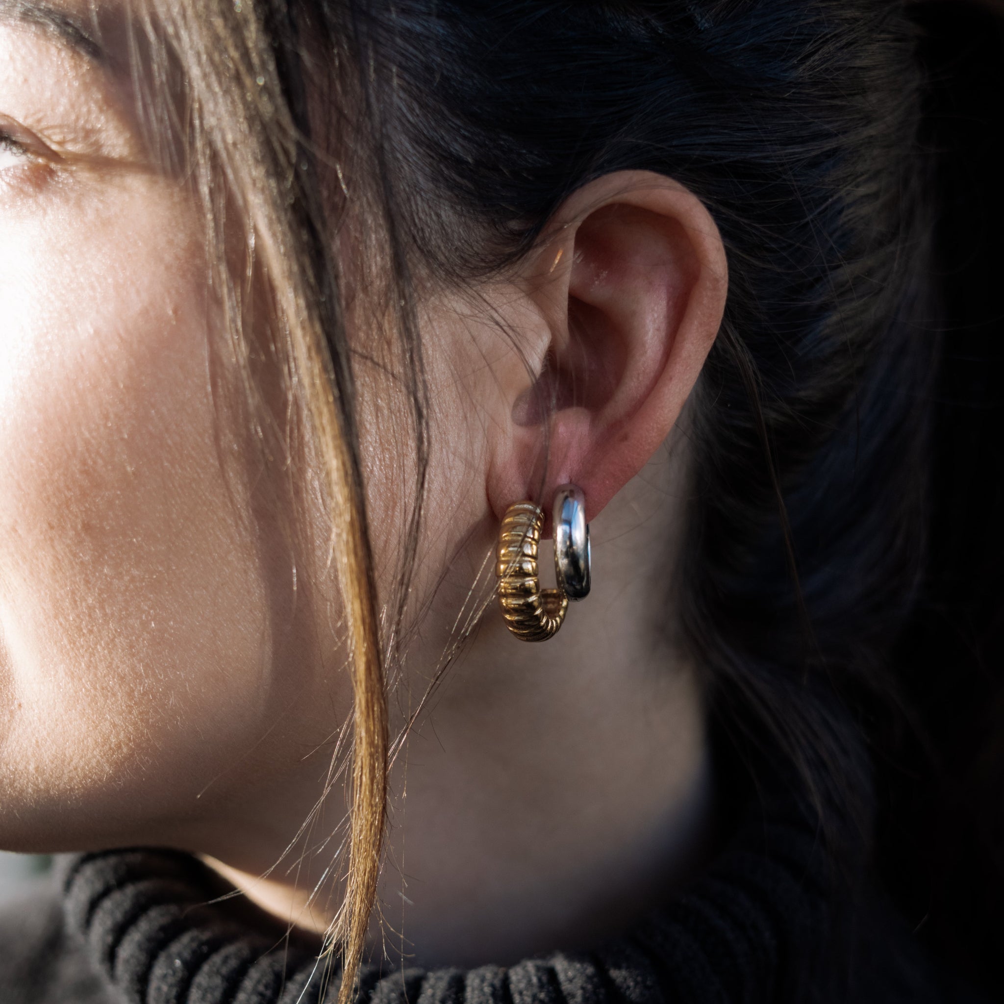Close-up of a person wearing gold hoop earrings with a blurred background