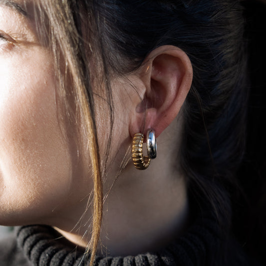 Close-up of a person wearing gold hoop earrings with a blurred background