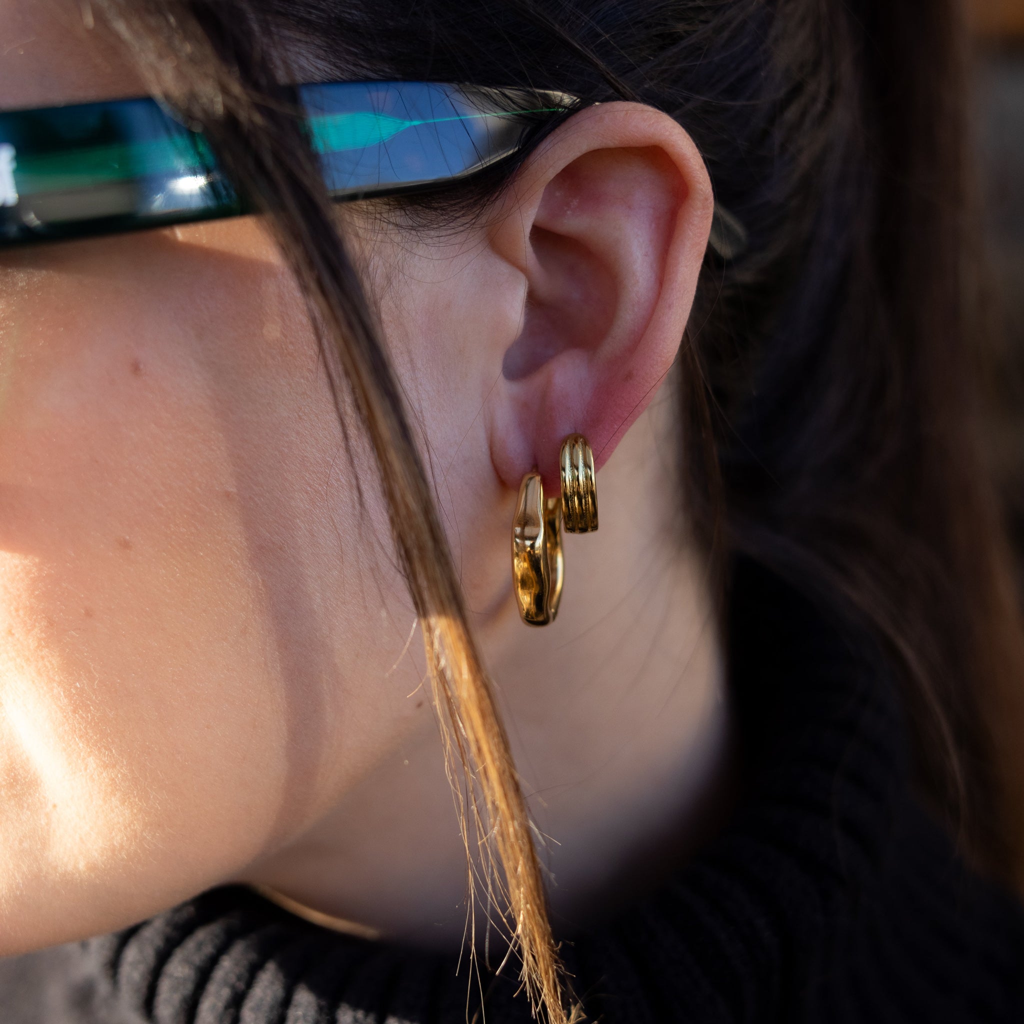 Close-up of a person wearing gold hoop earrings with blurred background