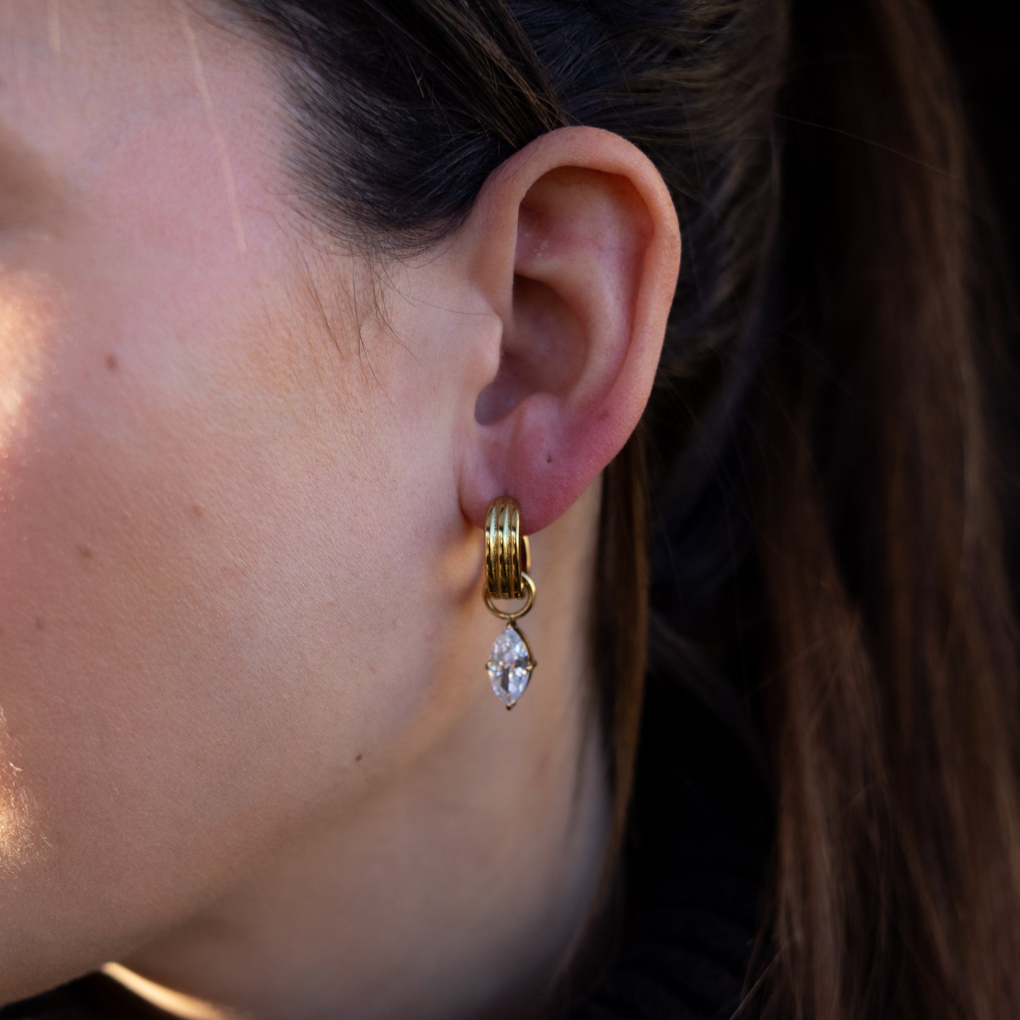 Close-up of a person wearing a gold earring with a clear gemstone.