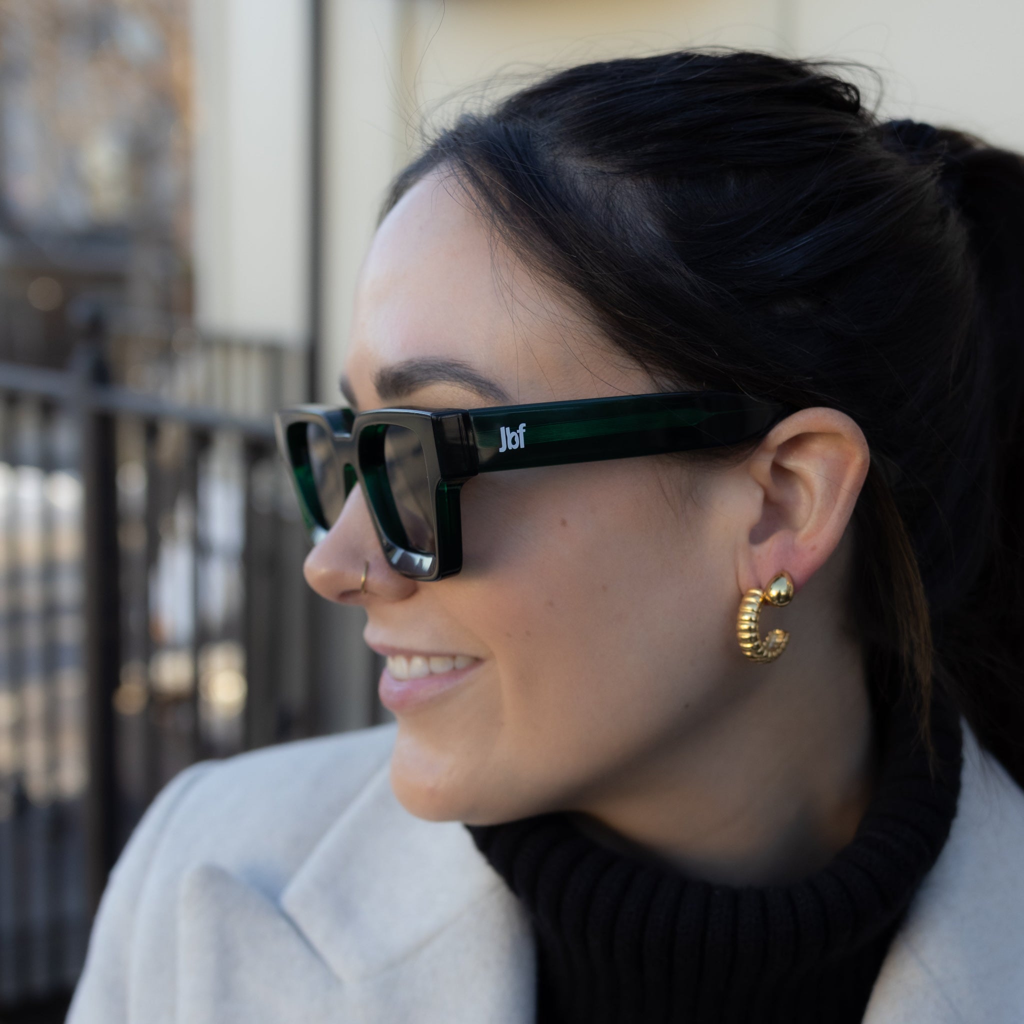 Woman wearing sunglasses and a coat, standing outdoors.