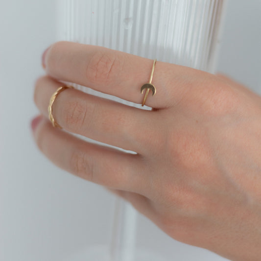 Hand wearing two gold rings with a blurred glass in the background
