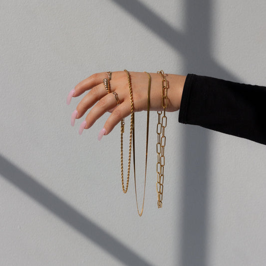 Hand wearing multiple gold chain bracelets on a light gray background
