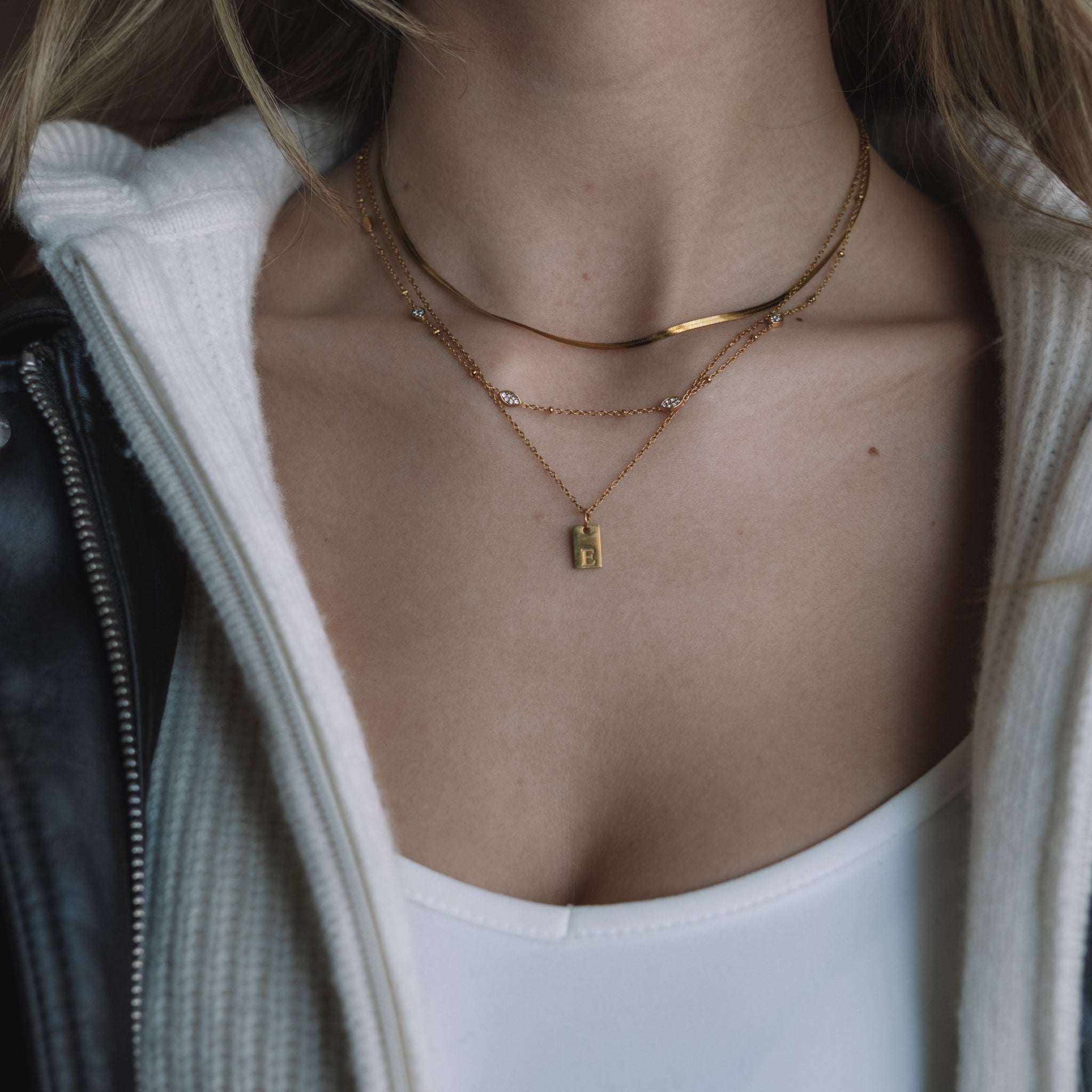 Person wearing a white top, black jacket, and gold necklaces with a neutral background