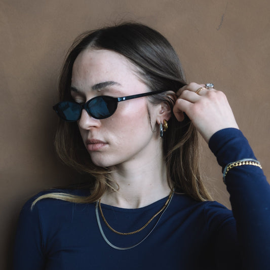 Woman wearing dark sunglasses and a blue top against a brown background