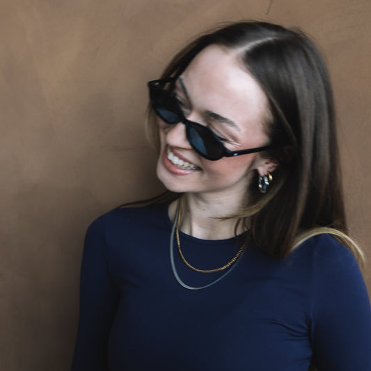 Woman wearing sunglasses and a dark blue top against a brown background