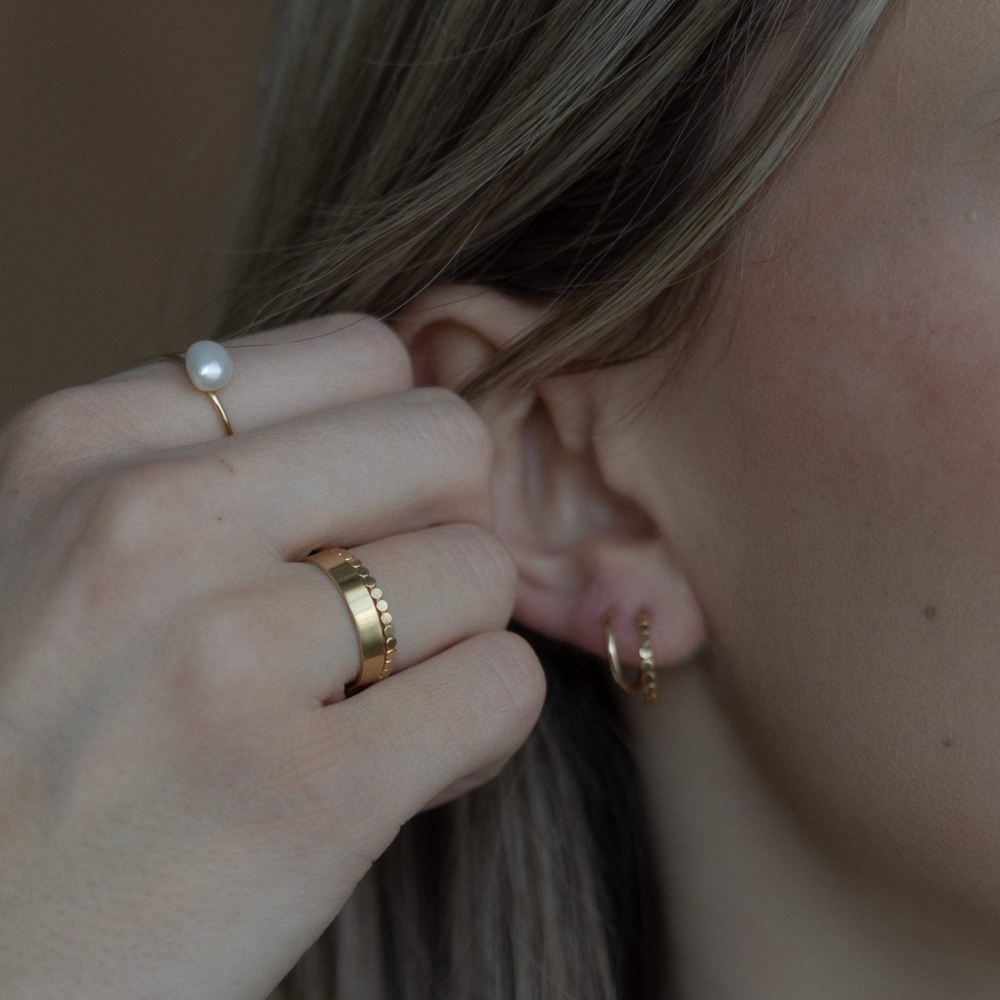 Close-up of a person wearing gold earrings and rings.