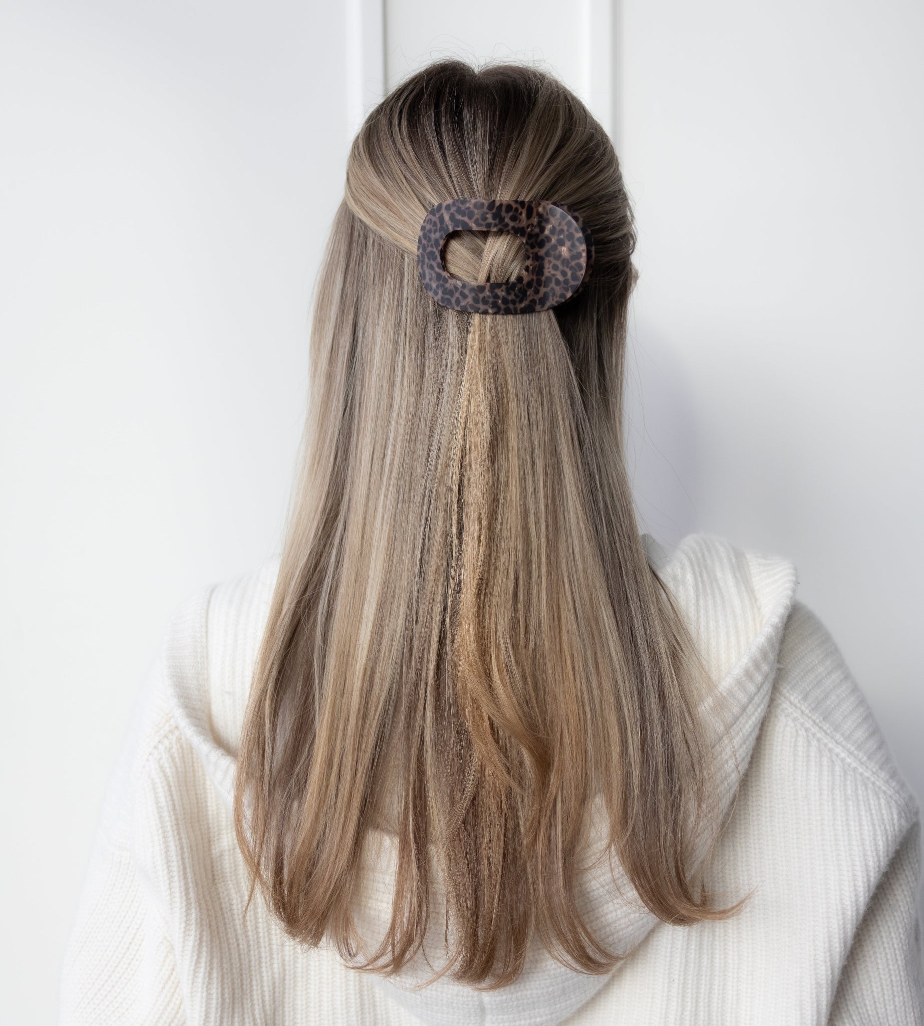 Person with long hair tied back using a decorative hair clip against a white background