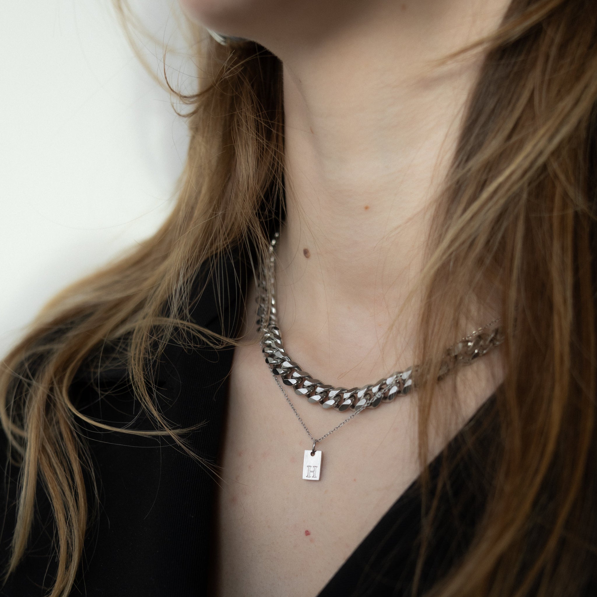 Close-up of a person wearing a silver chain necklace with a tag pendant.