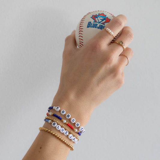 Hand holding a baseball with a visible brand logo, wearing multiple bracelets on a plain background