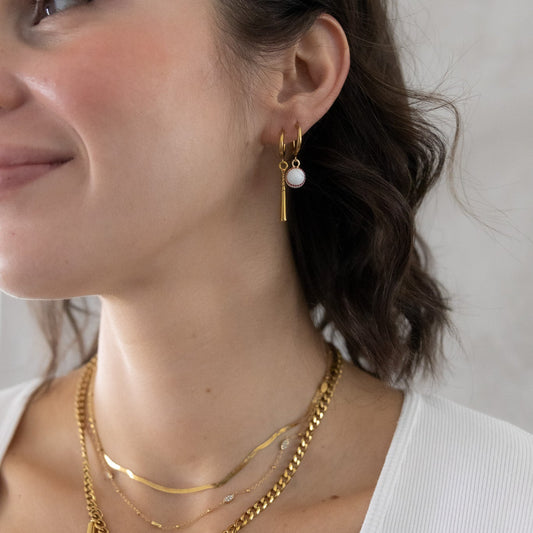 Woman wearing gold necklaces and earrings with a neutral background