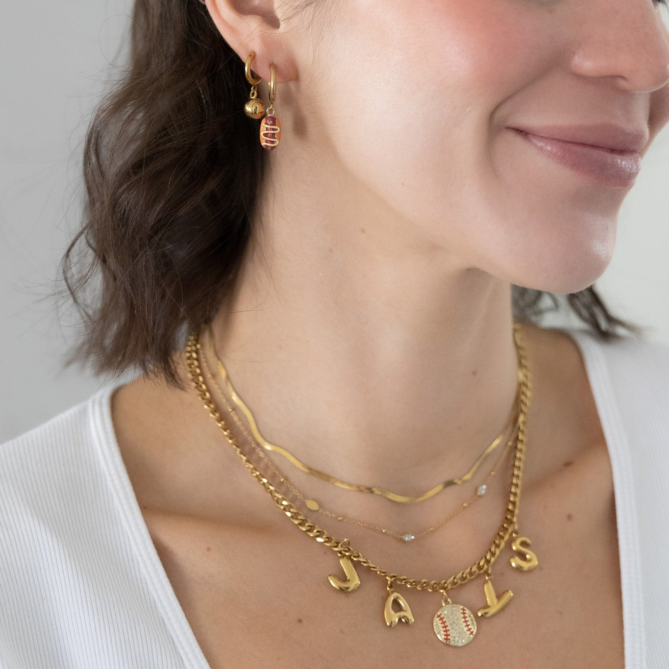 Woman wearing gold necklaces and earrings against a plain background