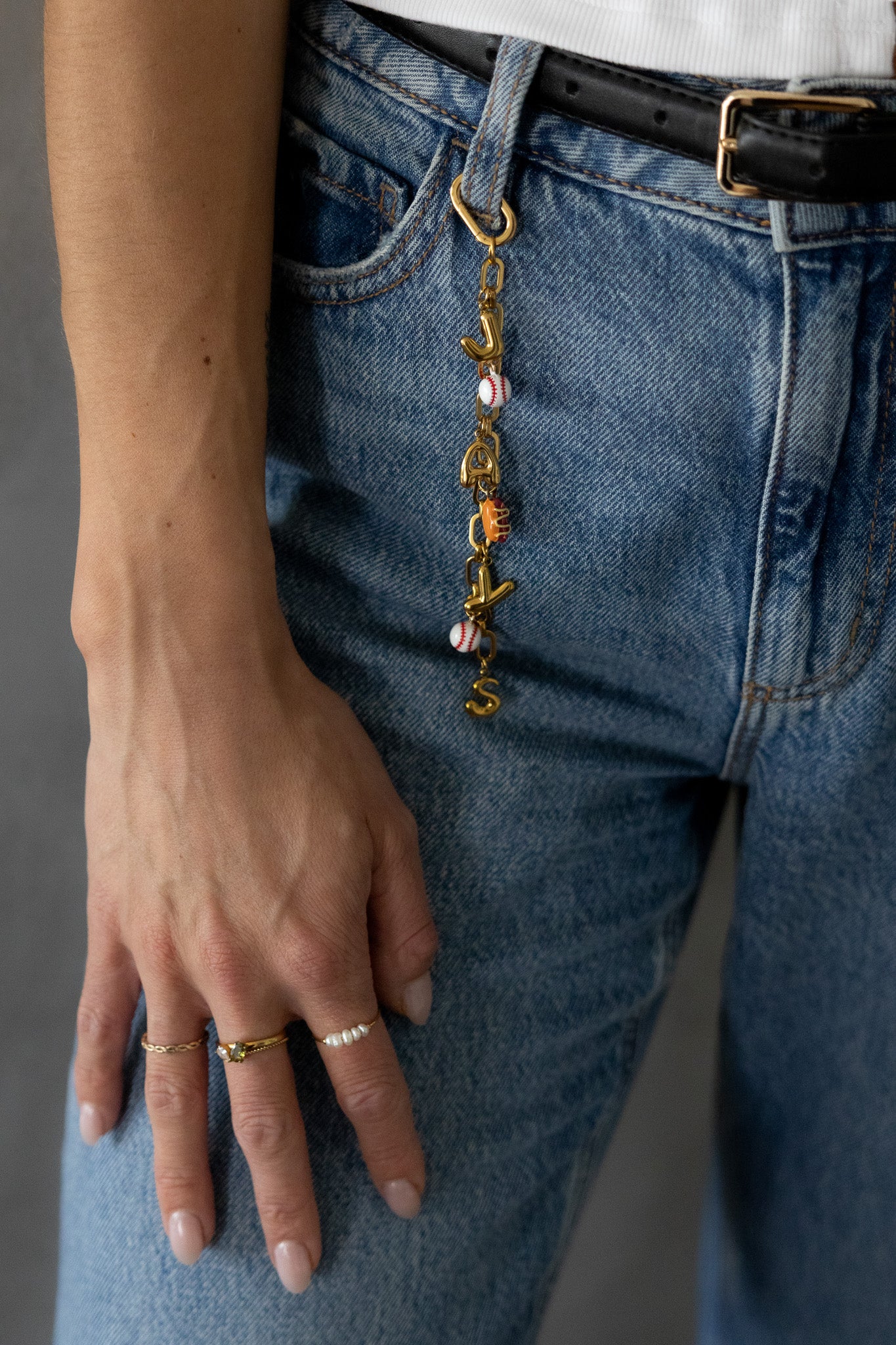 Person wearing blue jeans with a decorative keychain and rings on fingers.