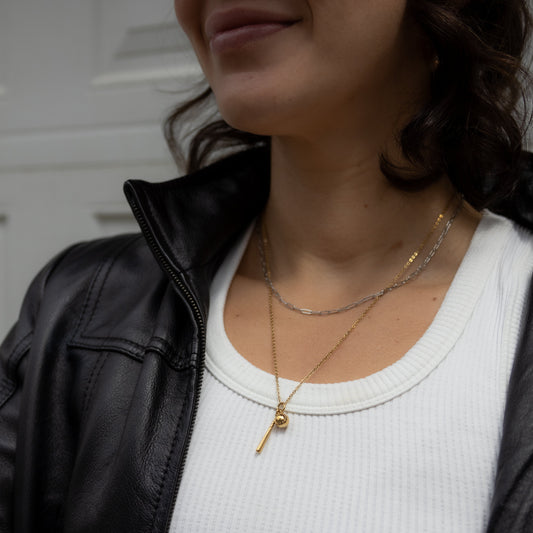 Person wearing a black jacket, white shirt, and gold necklaces with a blurred background