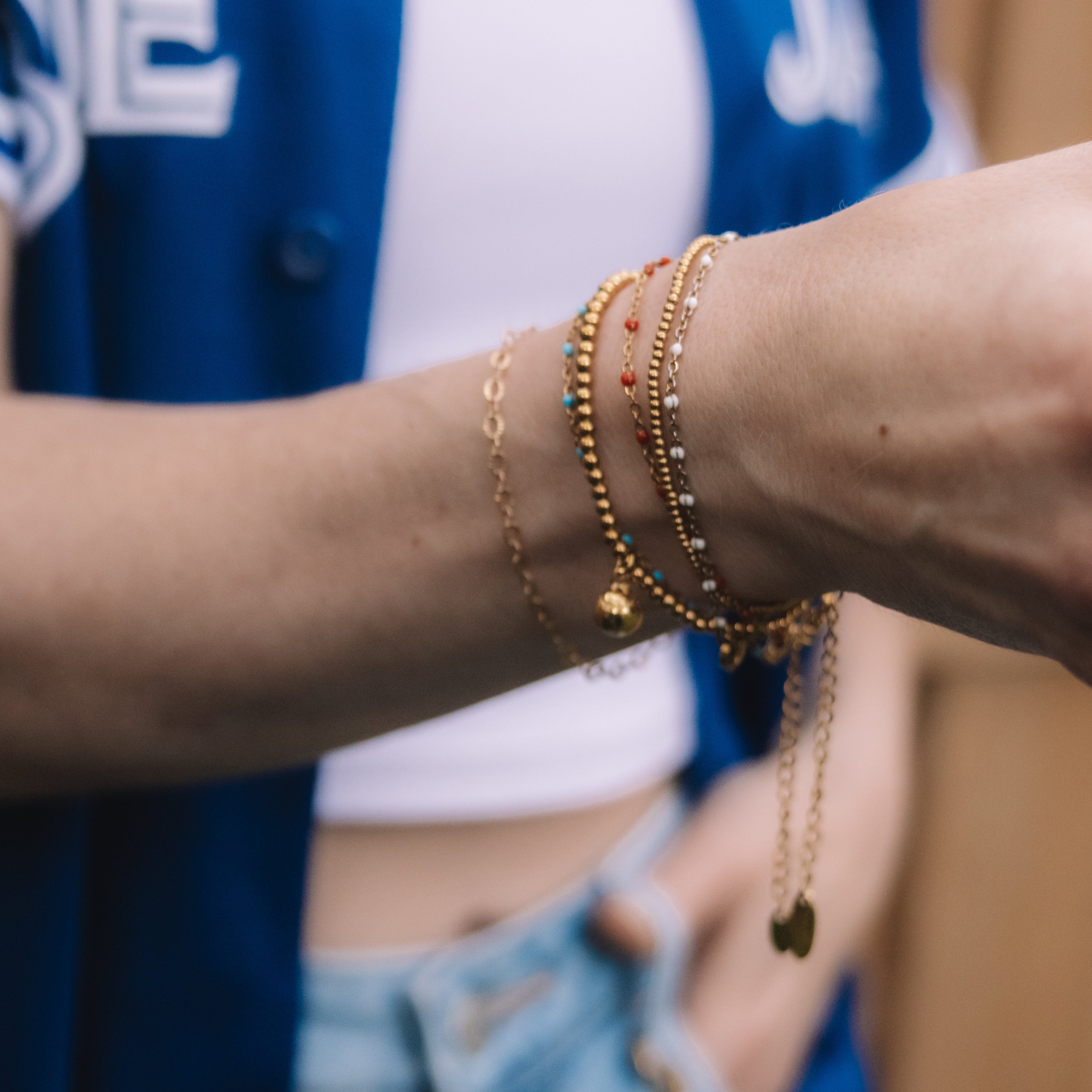 Close-up of a person wearing multiple gold bracelets on a blurred background