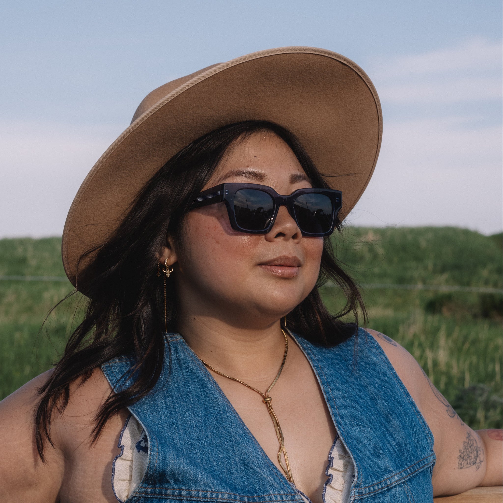 Woman wearing a wide-brimmed hat and sunglasses, standing in a field.