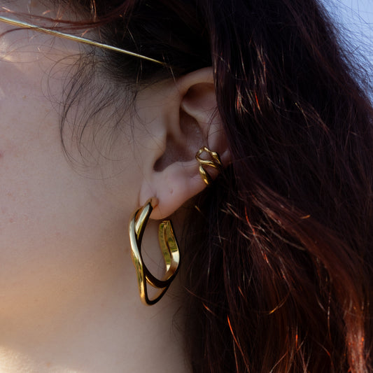 Close-up of a person wearing gold hoop earrings with hair and part of a necklace visible.