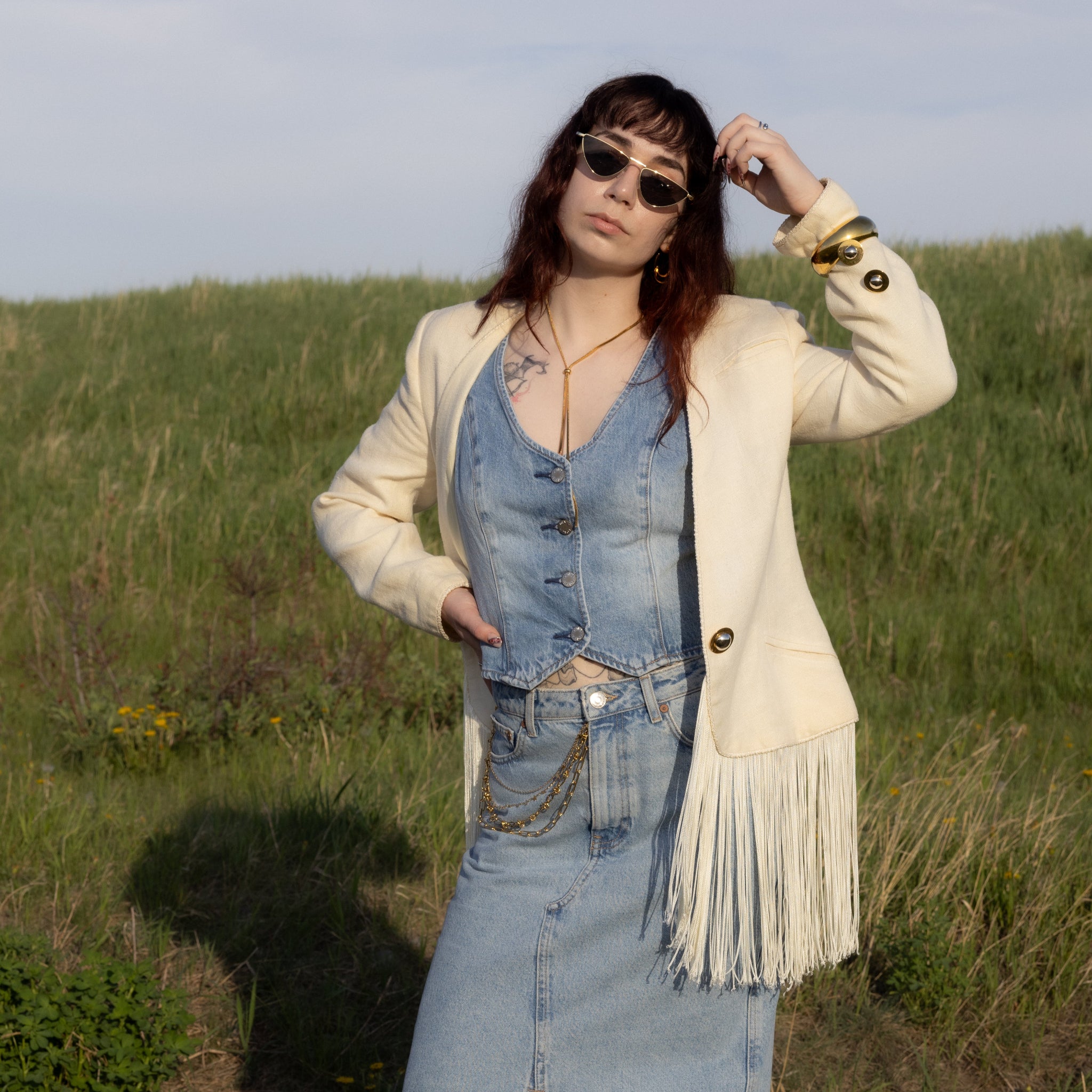 Woman in a denim outfit with a beige jacket standing in a grassy field.