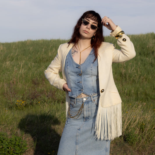 Woman in a denim outfit with a beige jacket standing in a grassy field.