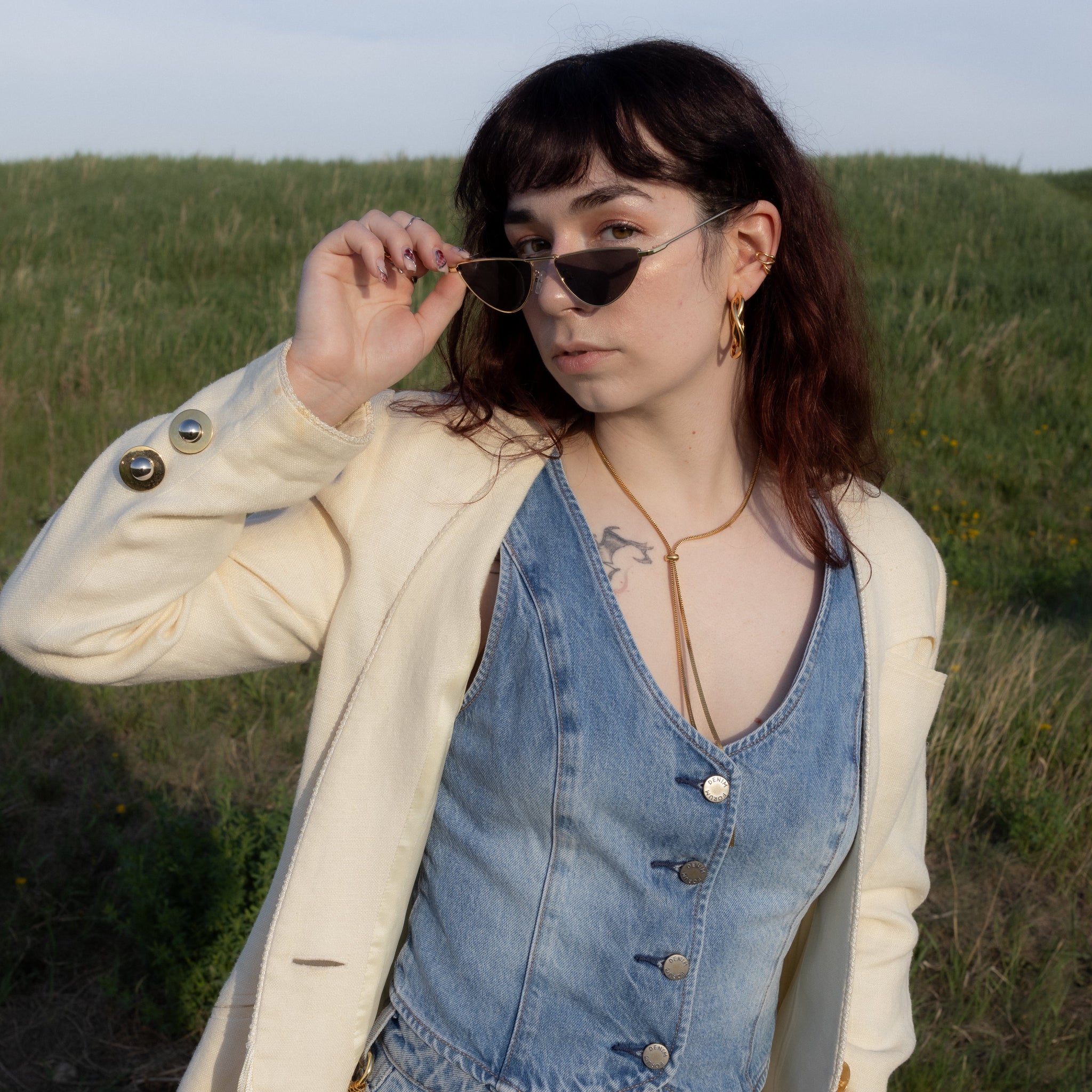 Woman wearing a denim dress and beige jacket in a grassy field